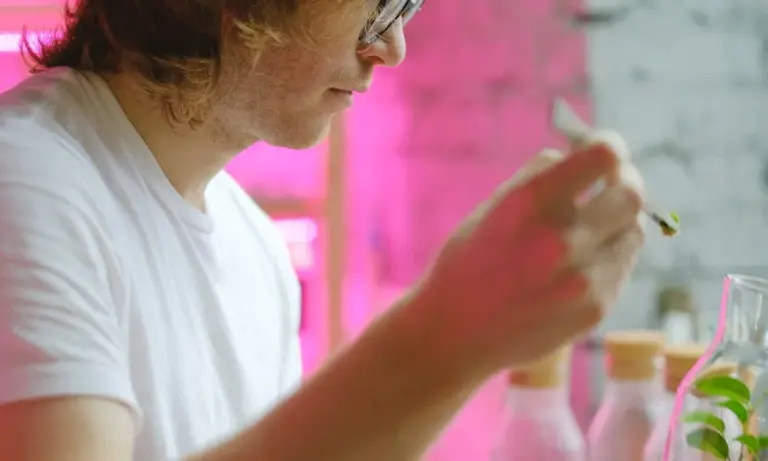 Side-profile of a person in a white shirt with pink ambient lighting indoors, holding a small object near their lips.