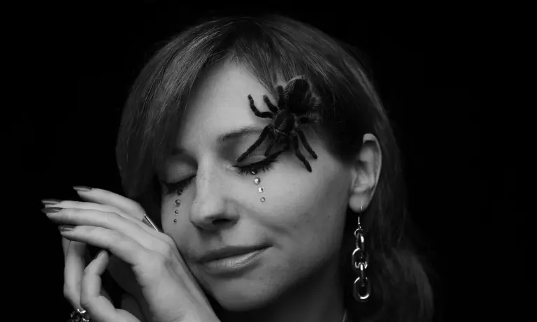 Black-and-white portrait of a woman with a tarantula perched near her eye.