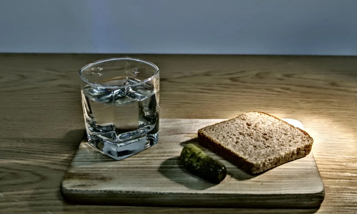Glass of water on a wooden board beside a slice of bread and a pickle, illustrating moisture context for tarantula care.