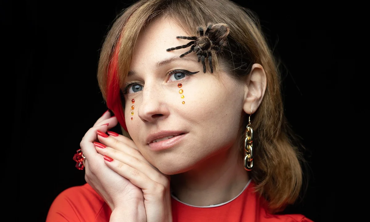 A person wearing a red top has a tarantula perched on their head, illustrating calm, controlled exposure to a pet tarantula.