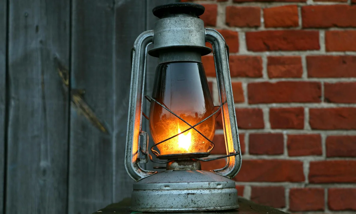 Old metal lantern with a glowing flame against a brick wall, representing a heat source for tarantula enclosures.