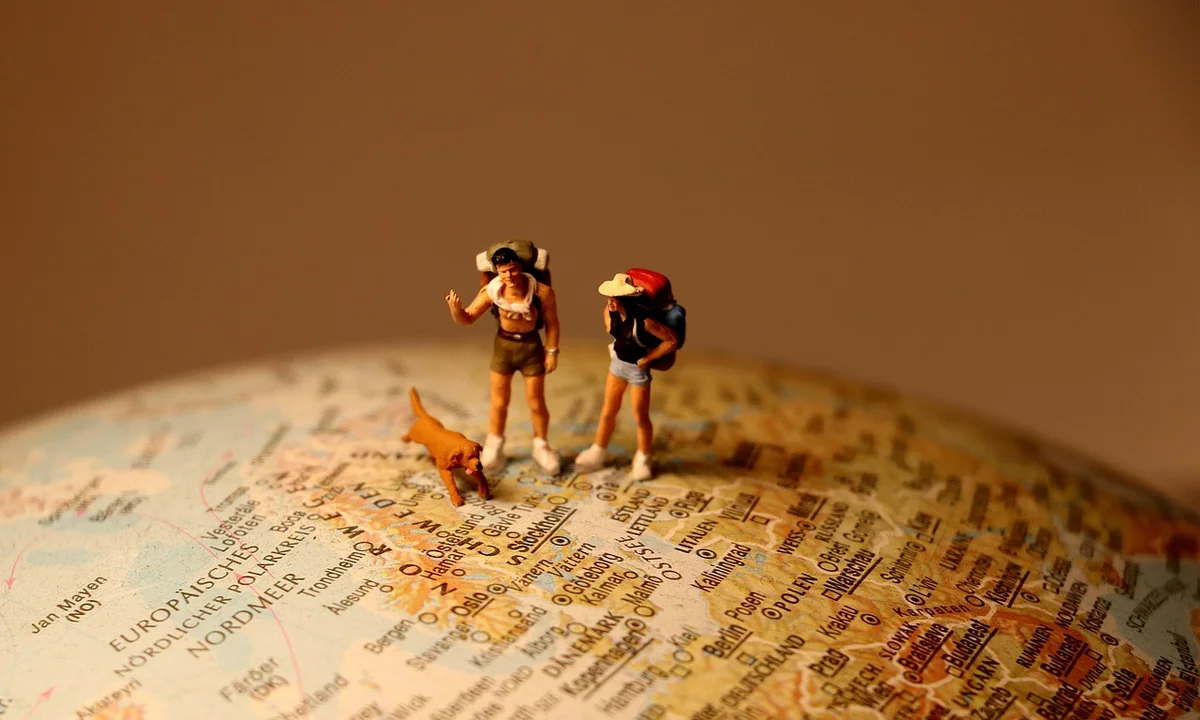 Two tiny hikers and a small dog standing on a world map, illustrating Old World tarantula regions across Africa, Asia, Europe, and the Middle East.