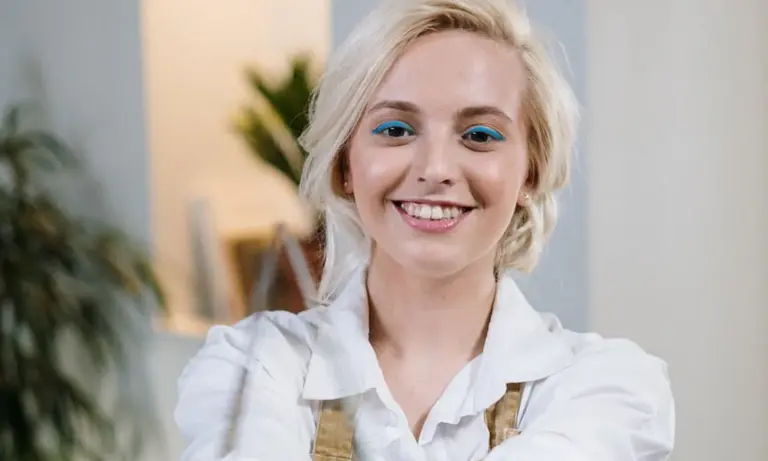 Smiling woman with blonde hair wearing a white shirt in a bright indoor setting