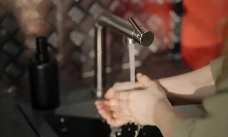 Hands under a running faucet with water streaming into a sink