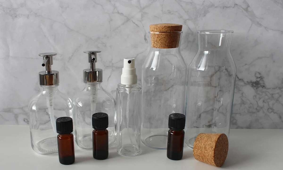 Assorted glass bottles and spray pumps containing cleaning solutions arranged on a marble surface, illustrating common household scented cleaners and air fresheners.