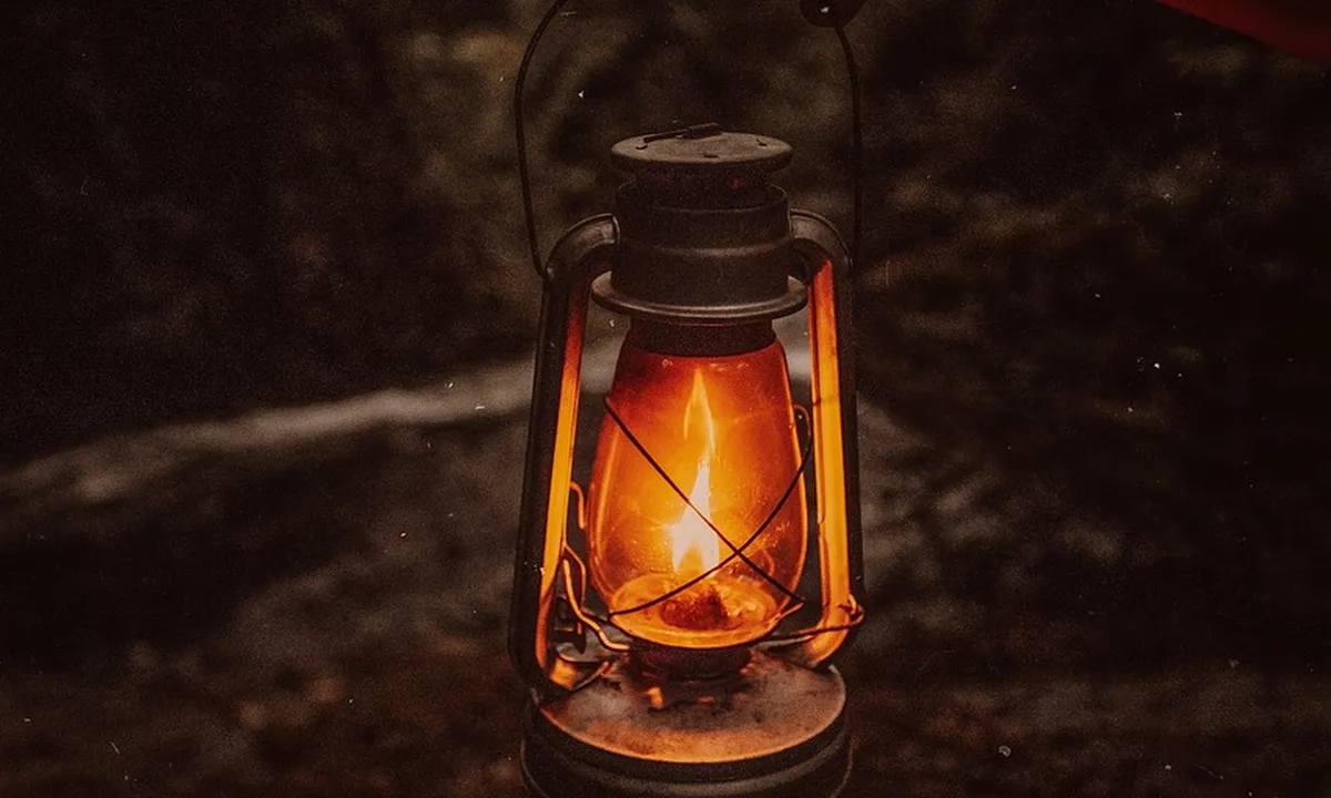 A lit vintage lantern glowing with an orange flame in a dark setting, illustrating non-lamp heating concepts for tarantula enclosures.