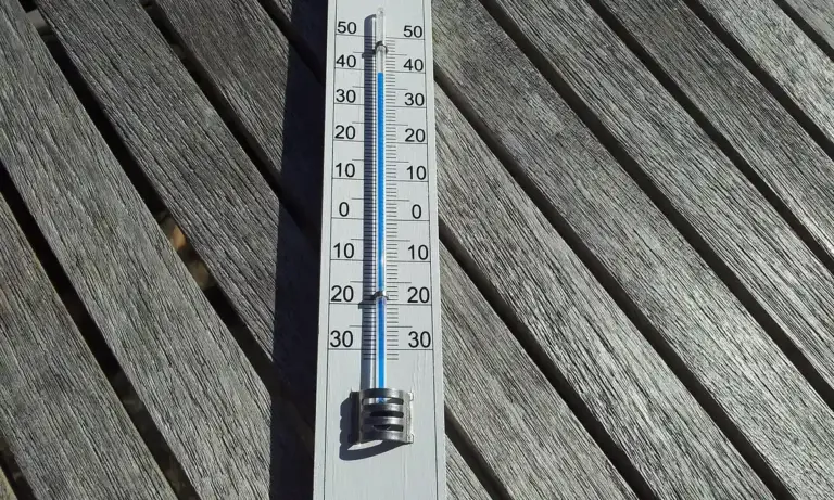Close-up of a thermometer resting on weathered wooden planks, showing a temperature scale.